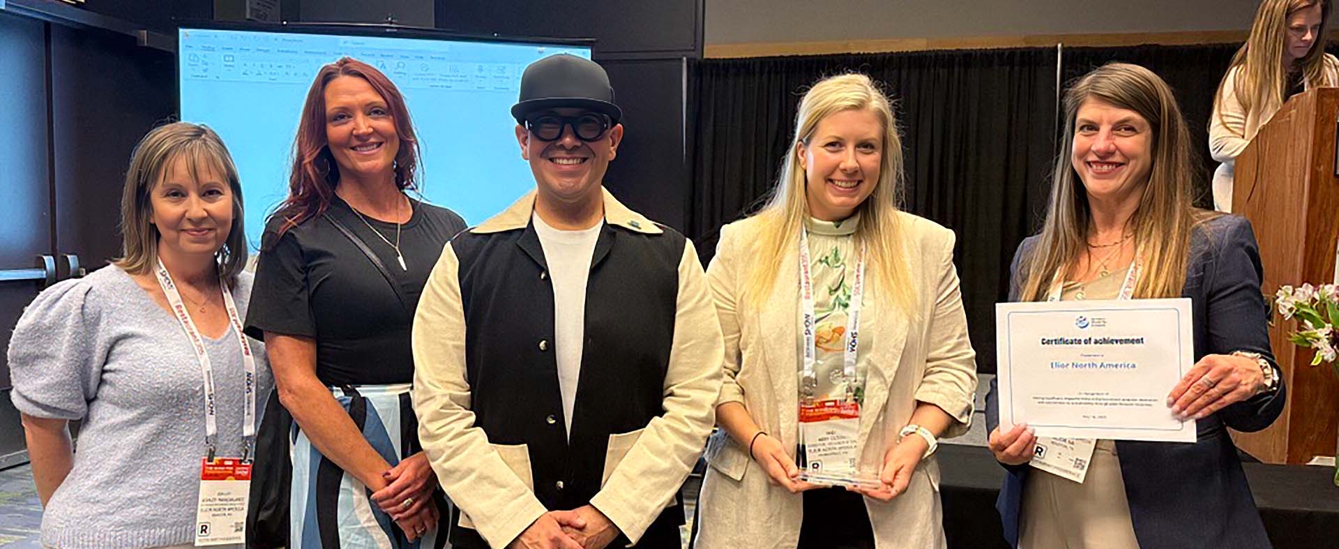 Five Elior North America team members celebrate an industry award at a conference, proudly displaying a recognition trophy and certificate of achievement.