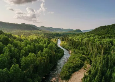 Lush green forests and a winding river surrounded by mountains, representing Elior North America’s commitment to environmental sustainability, natural resource conservation, and protecting the planet.