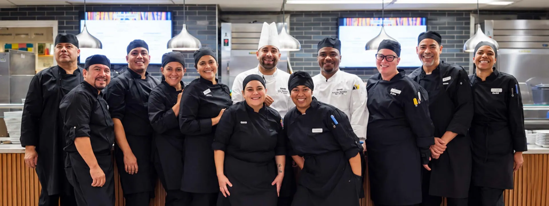 Elior North America culinary team members smiling together in a commercial kitchen, showcasing careers in food service, dining, and hospitality.