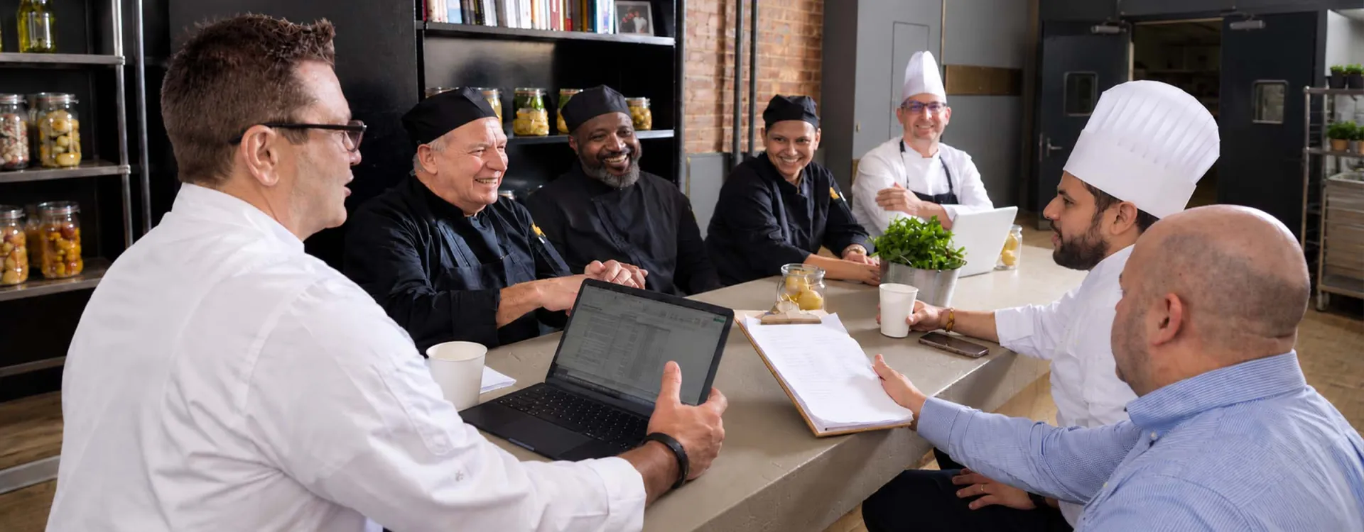 Elior North America culinary professionals and leadership team collaborating in a commercial kitchen, reflecting teamwork and a commitment to exceptional foodservice.