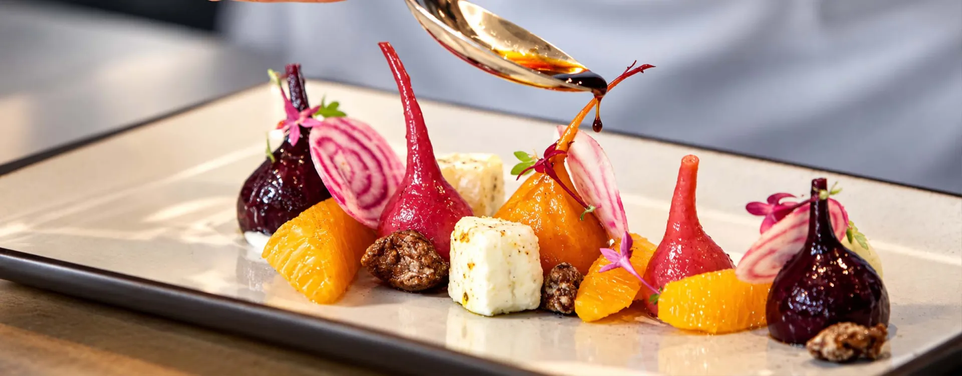 Chef finishing an elegantly plated gourmet dish featuring roasted beets, citrus, artisan cheese, and edible flowers, showcasing fine dining and culinary excellence for special events.
