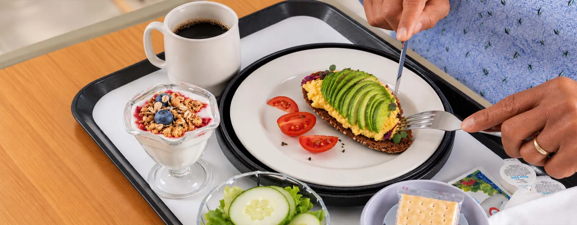 Patient enjoying a freshly prepared, nutritious breakfast featuring avocado toast, fresh fruit yogurt, and vegetables, highlighting Elior North America's healthcare and senior living dining services.