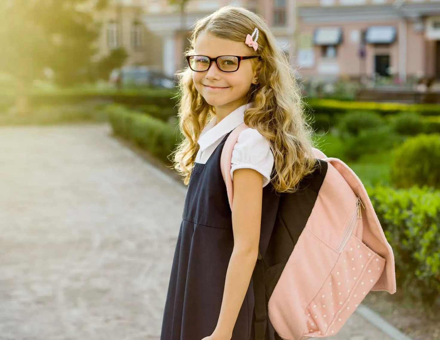 School age girl in uniform smiling at camera while entering school grounds