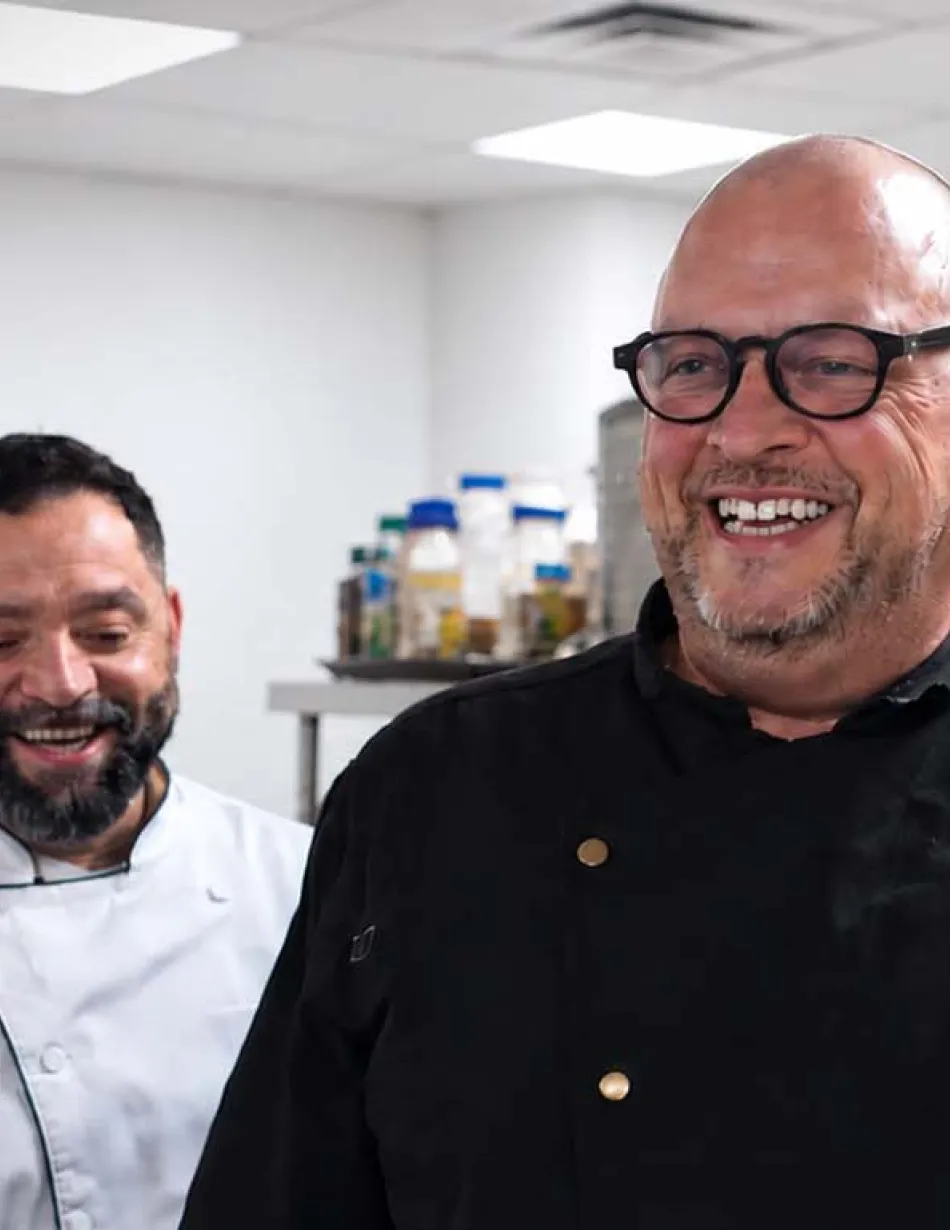 Two smiling chefs in a clean, modern commercial kitchen, showcasing professional culinary expertise and foodservice operations.