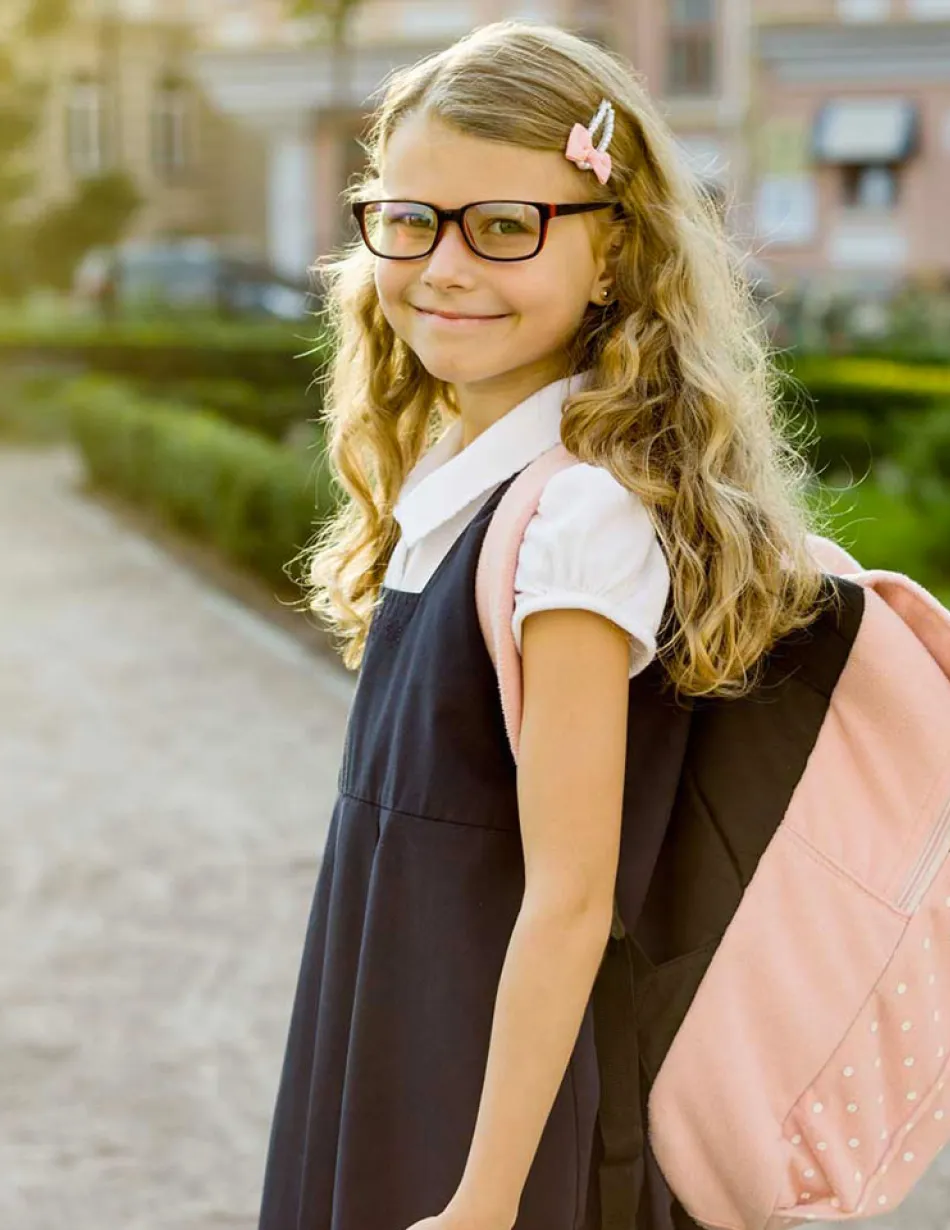 School age girl in uniform smiling at camera while entering school grounds