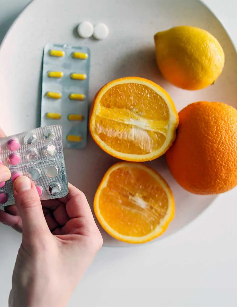 Hand holding medication with bowl of oranges and medicine in the background