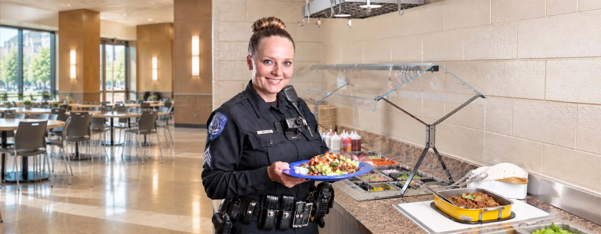 Sheriff's deputy holding a freshly prepared meal beside a buffet station in a courthouse dining area, highlighting nutritious foodservice for corrections personnel.