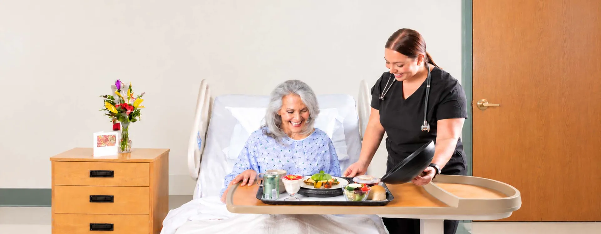 Healthcare professional serving a freshly prepared, nutritious meal to a smiling hospital patient, highlighting Elior North America's patient dining and healthcare food service solutions.