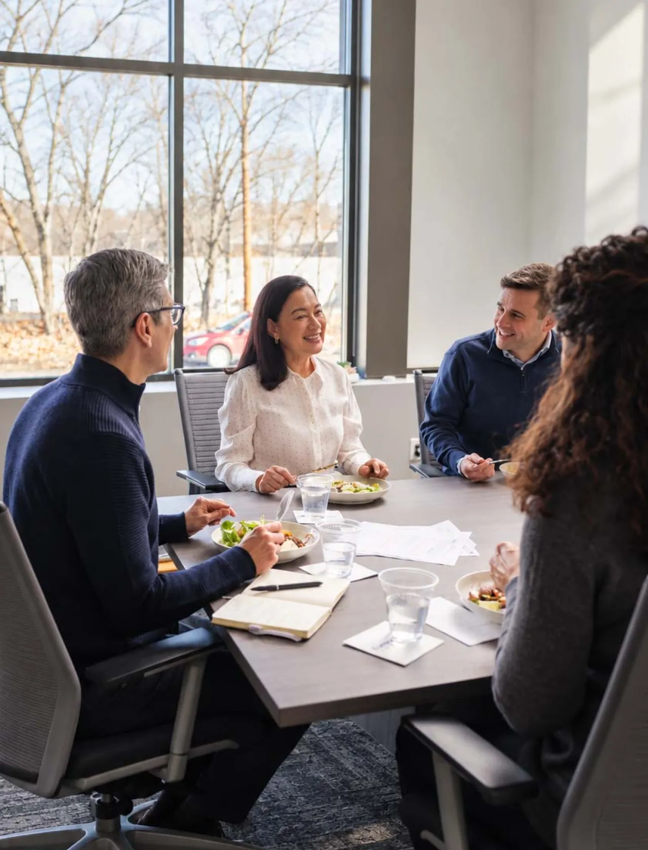 Four Elior North America team members share a meal and conversation around a table in a bright, modern workplace.