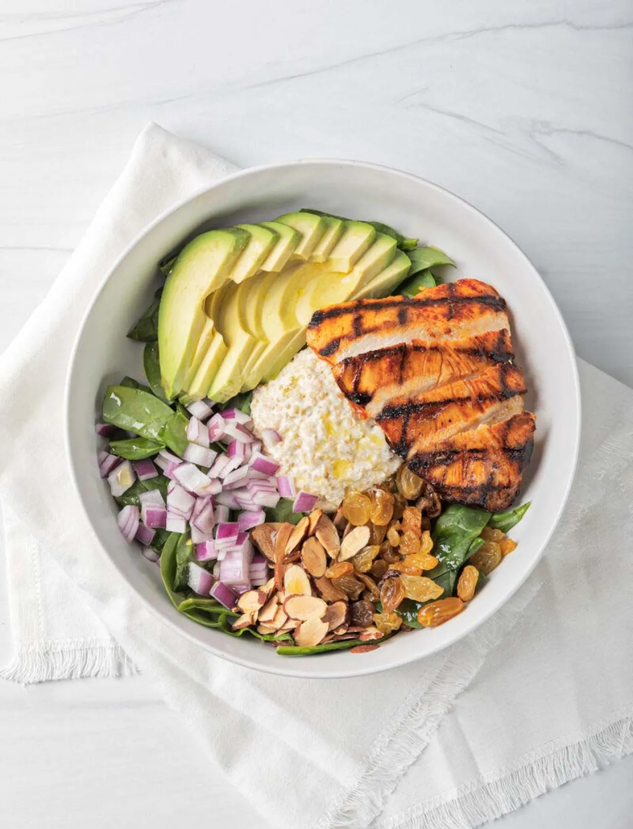 Grilled chicken and avocado salad bowl with fresh spinach, cottage cheese, red onions, sliced almonds and golden raisins, showcasing nutritious, balanced dining options from Elior North America’s BeWell program.