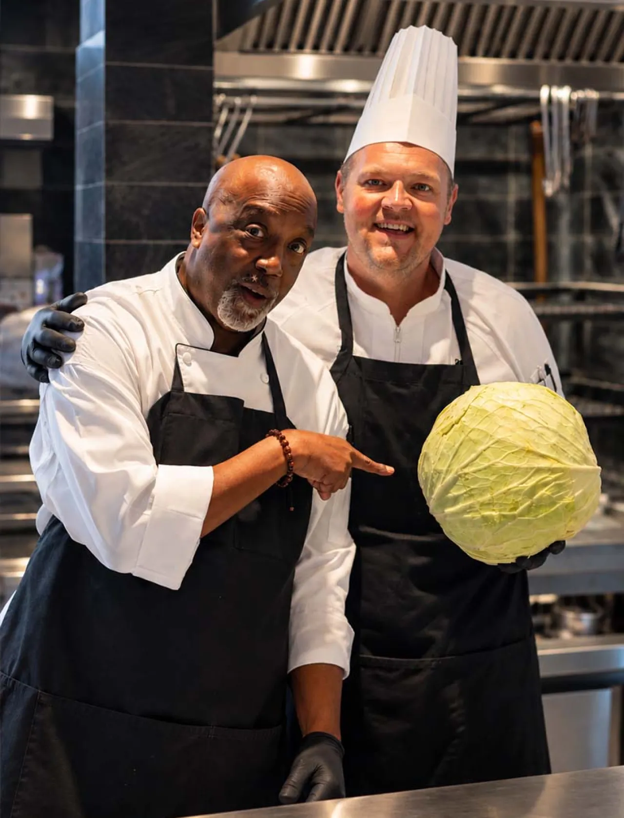 Two Elior North America chefs showcase fresh ingredients in a professional kitchen, reflecting culinary creativity, collaboration, and a passion for creating memorable food experiences.