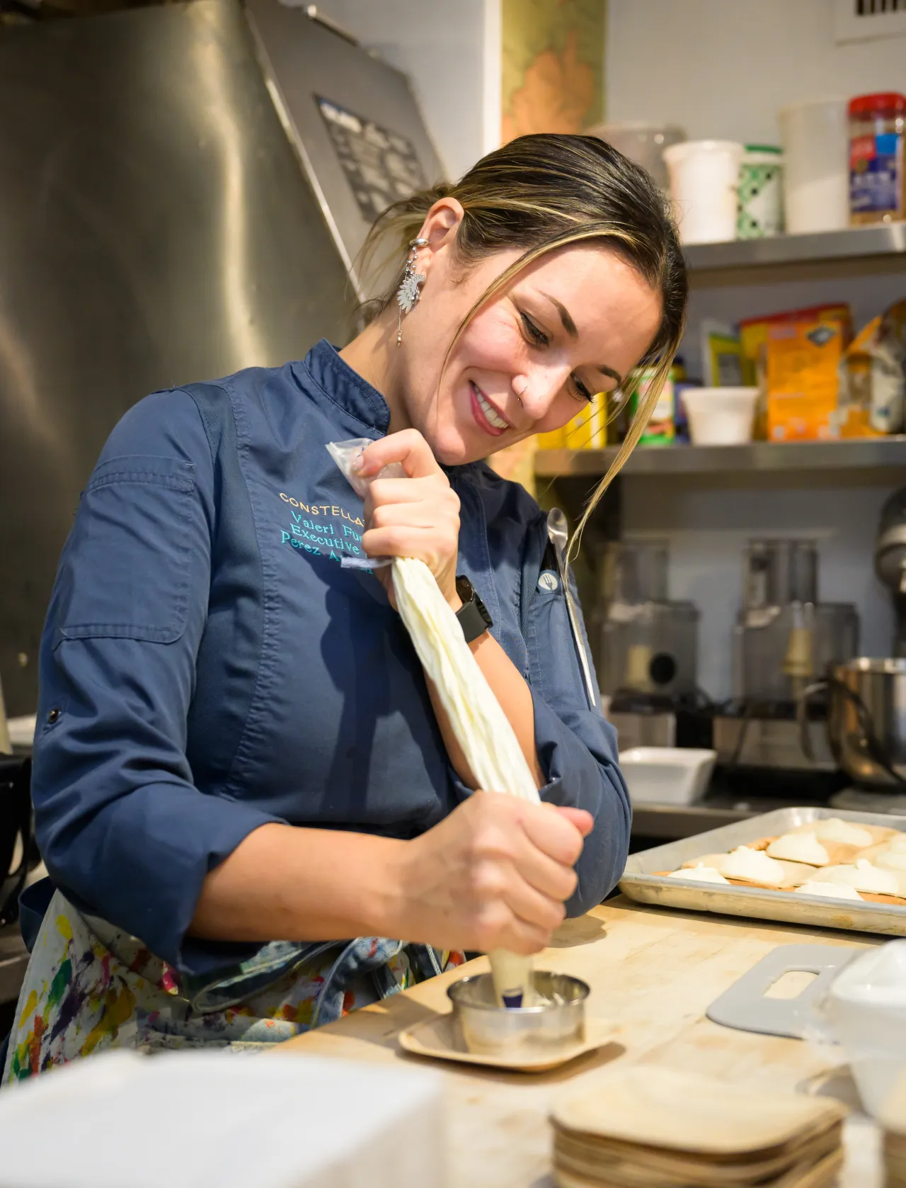 Chef Valeri Fuentes smiling while using piping bag to assemble a dish